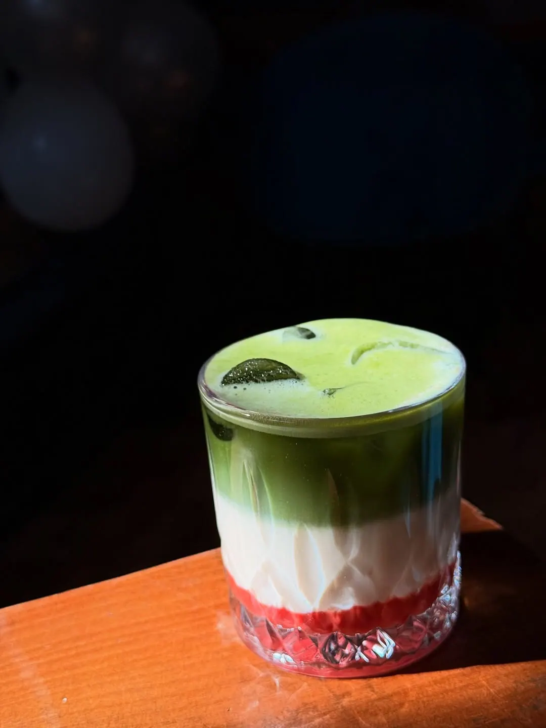 A layered iced green drink served in a tall glass on a wooden table.