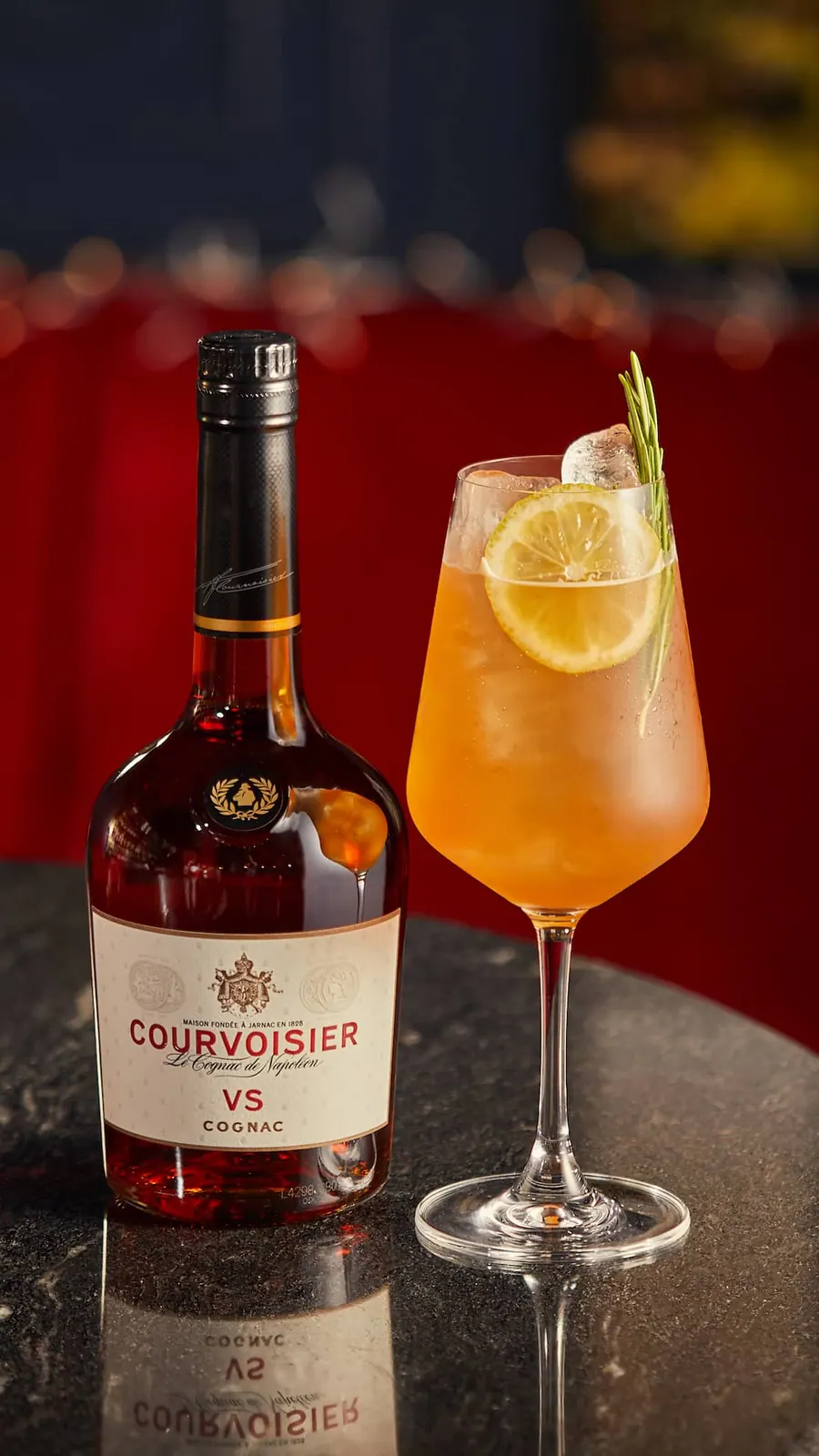 A cognac cocktail lit against a deep red backdrop on the bar.