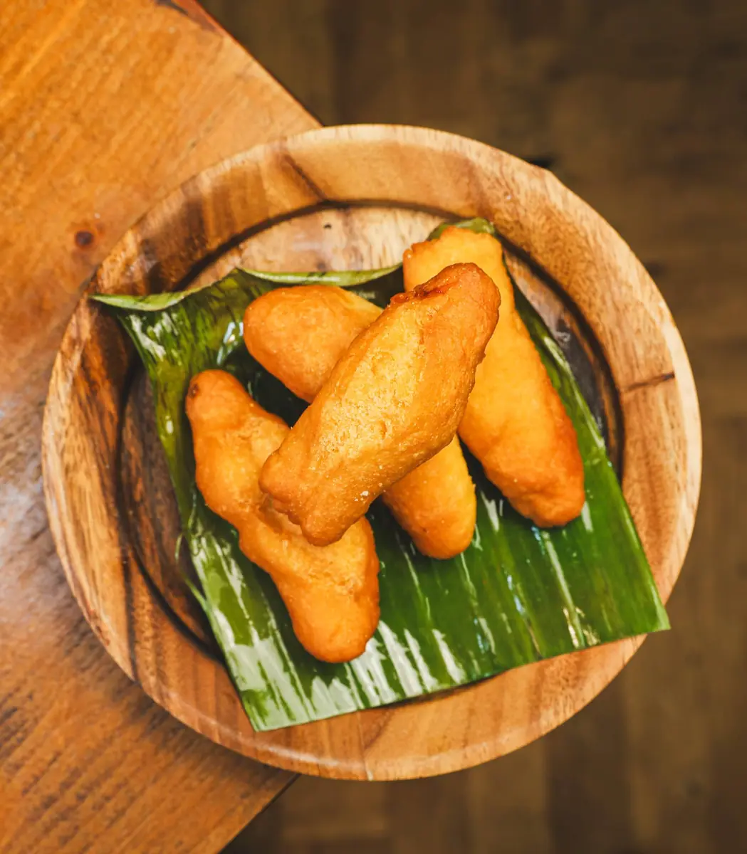 Golden fried dumplings served on a banana leaf in a wooden bowl.