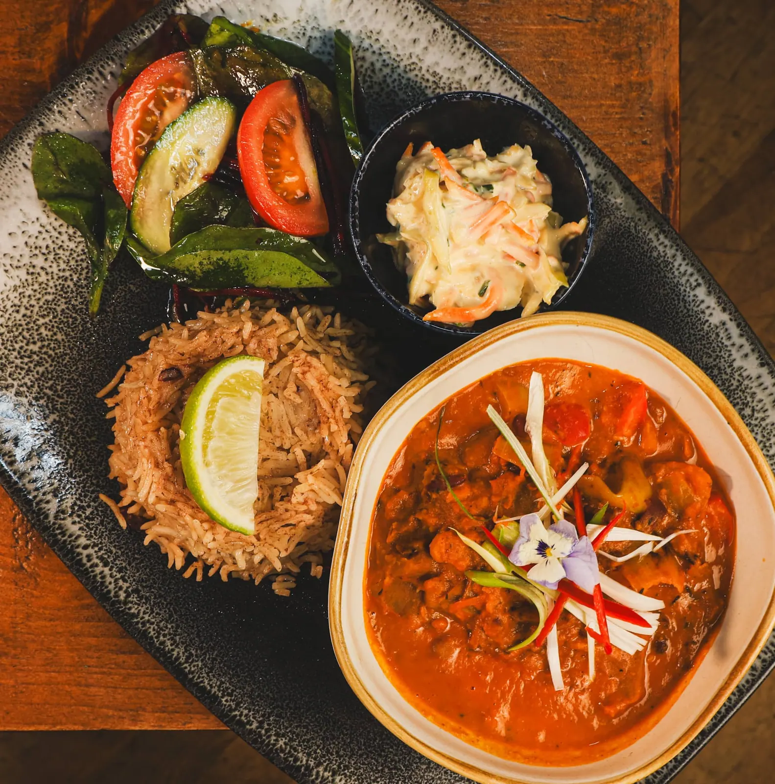 A Caribbean main course plated with rice and peas, side salad and coleslaw.