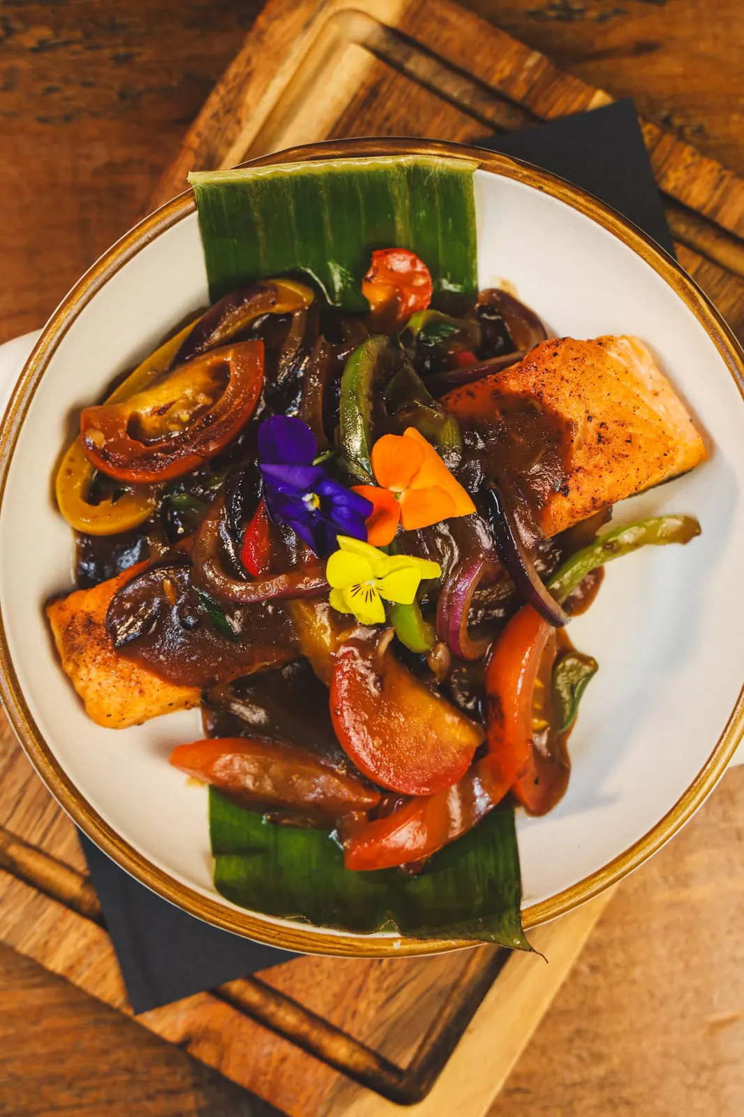 Grilled fish with peppers and herbs, plated on a banana leaf.